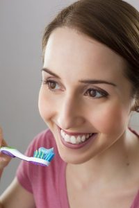 cepillo con dentrífico y mujer sonriendo.- Mujeres peor salud bucodental